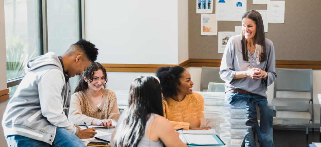 The professor engages with her students and they all laugh about a funny idea.