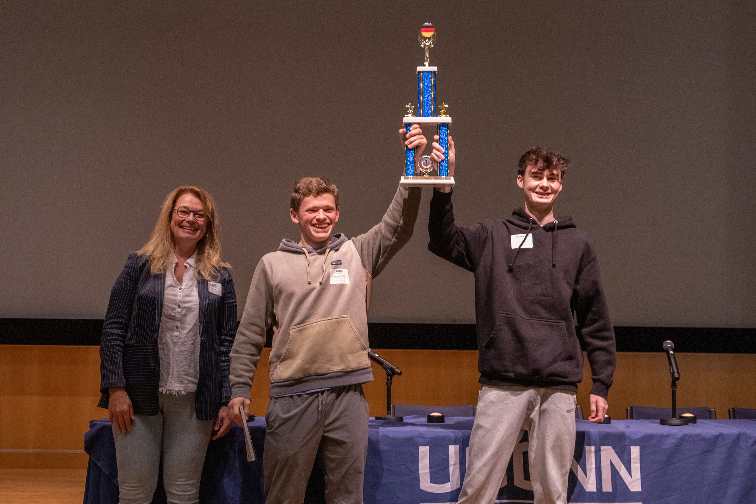 Two high school students hold up a trophy next to a professor